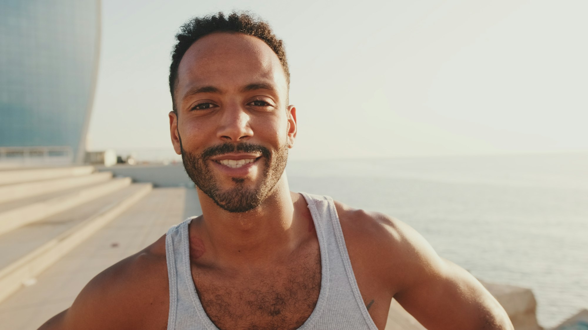 Close-up of bearded male fit athlete looking at camera and smiling while standing on the embankment